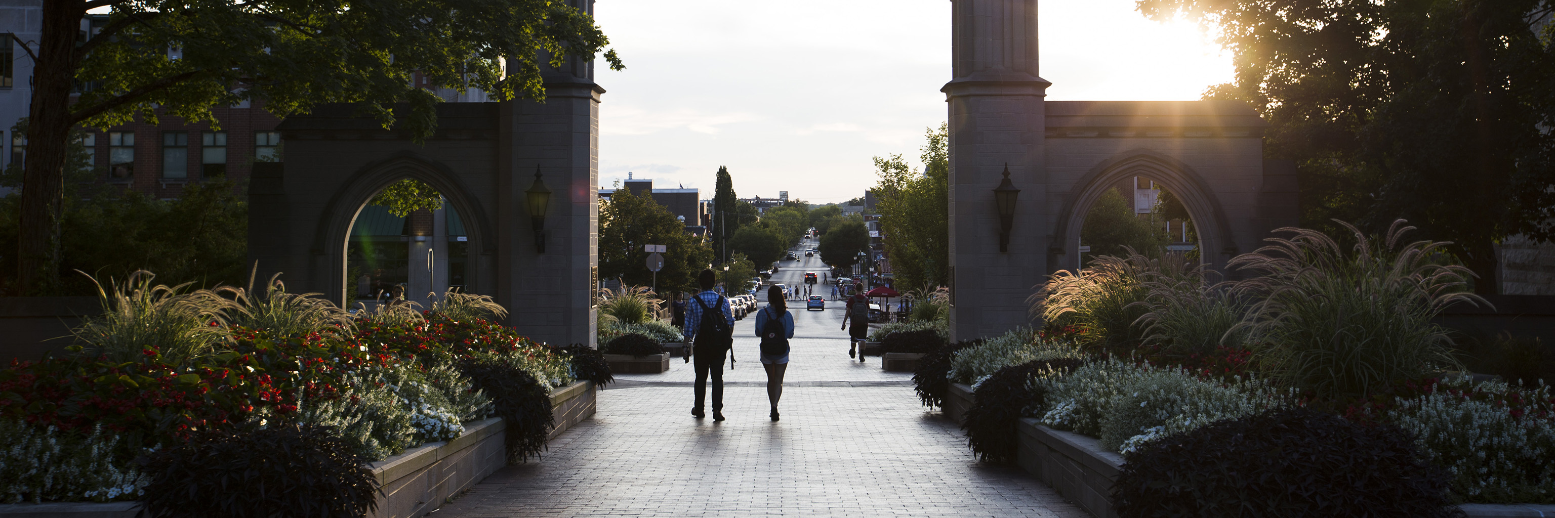 Two students walking past the Sample Gates toward Kirkwood Avenue at sunset.