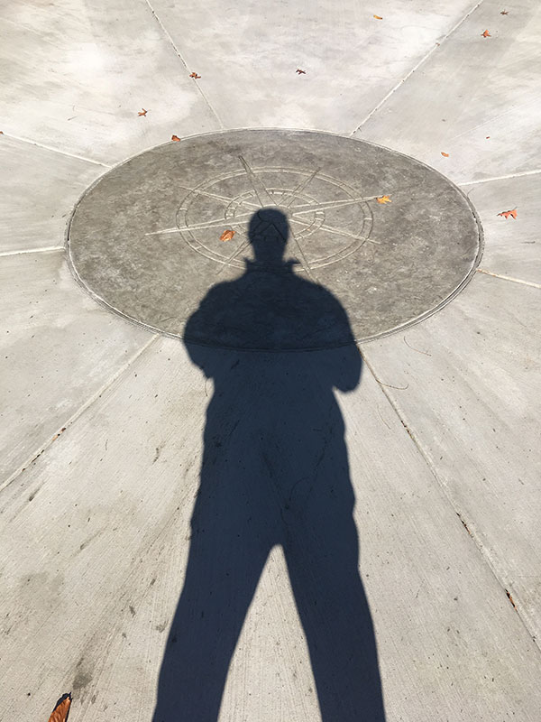 A person's shadow casts across a sundial on the ground.