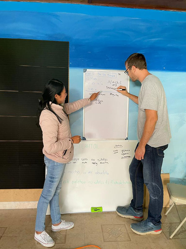 Two people point to terms on a white board, which is attached to a bright blue wall.