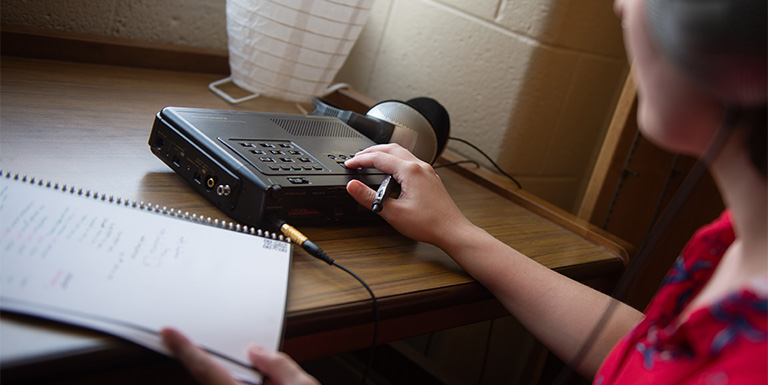 Close-up of a student taking notes while using audio lab equipment.