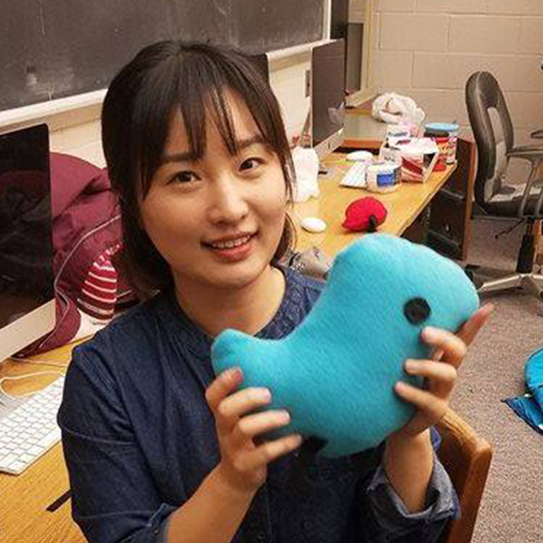 A woman smiles with a blue plush bird toy.